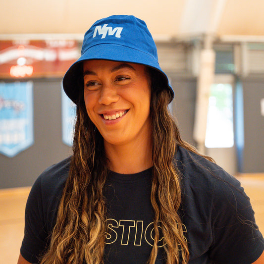 Person wearing a blue bucket hat and black t-shirt with 'MYSTICS' text indoors.